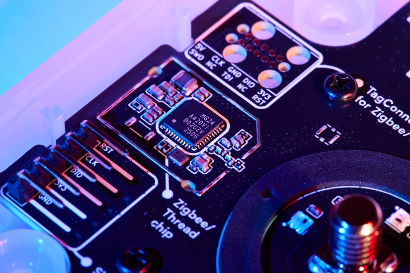A close-up macro shot of a the Zigbee/Thread chip (MG24) on a black printed circuit board, illuminated by dramatic blue and pink lighting.